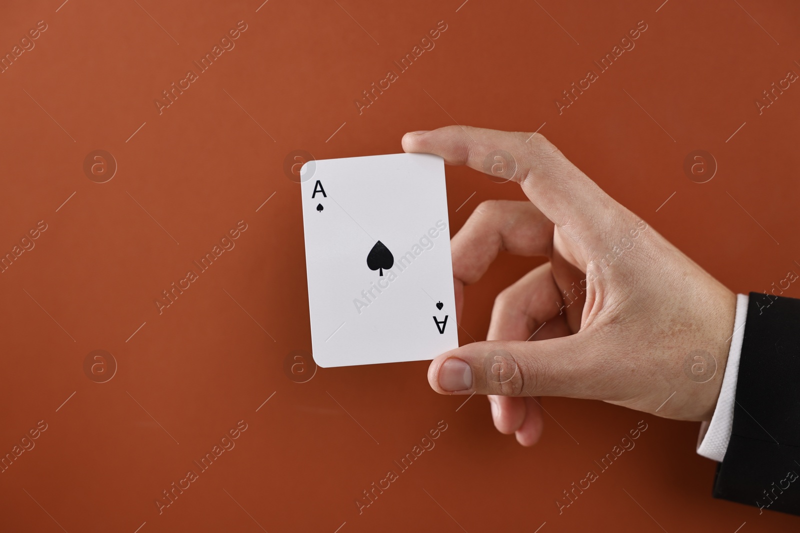 Photo of Illusionist showing playing card on dark orange background, closeup. Space for text