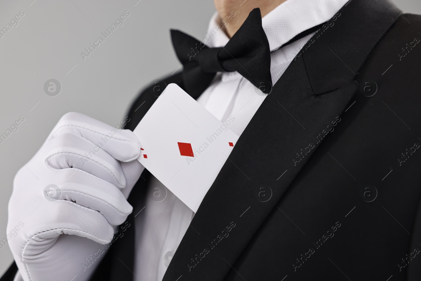 Photo of Illusionist hiding playing card behind jacket lapel on grey background, closeup