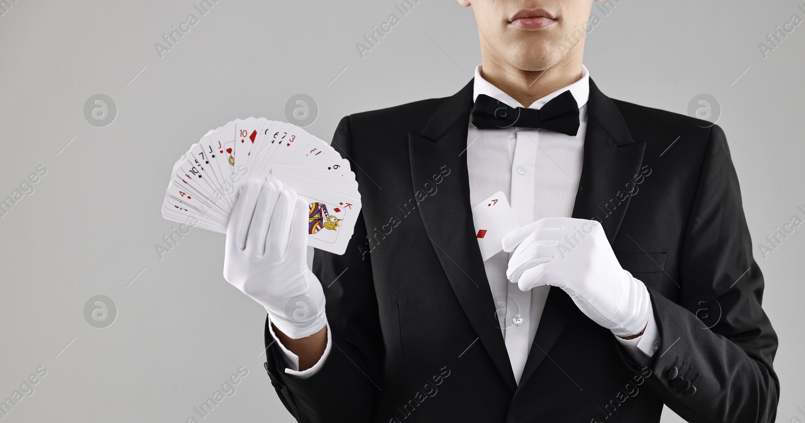 Photo of Illusionist hiding one playing card behind jacket lapel while showing deck on grey background, closeup. Space for text