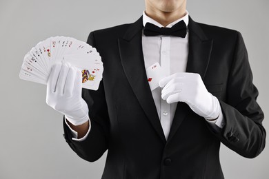 Photo of Illusionist hiding one playing card behind jacket lapel while showing deck on grey background, closeup