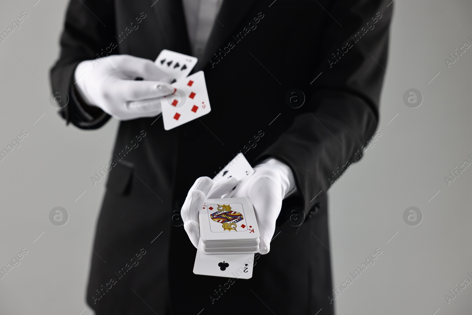 Photo of Illusionist showing trick with playing cards on grey background, closeup