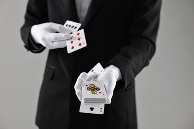 Photo of Illusionist showing trick with playing cards on grey background, closeup