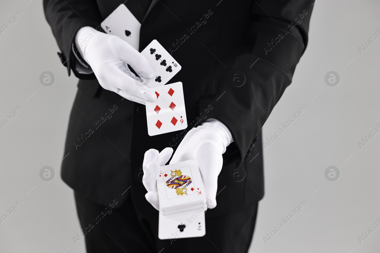 Photo of Illusionist showing trick with playing cards on grey background, closeup