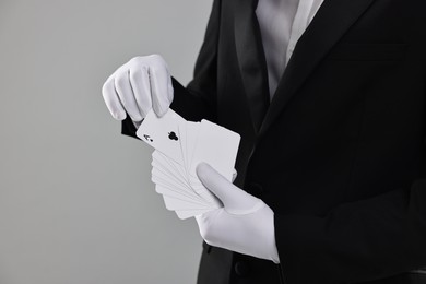 Photo of Illusionist taking one playing card from deck on grey background, closeup. Space for text