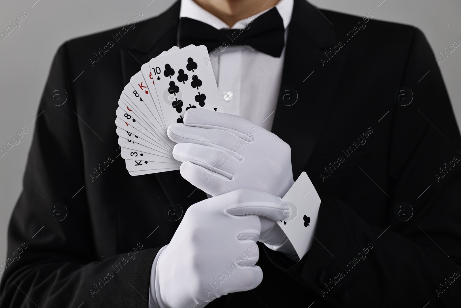 Photo of Illusionist hiding one playing card up his sleeve while showing deck on grey background, closeup