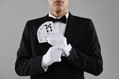 Photo of Illusionist hiding one playing card up his sleeve while showing deck on grey background, closeup