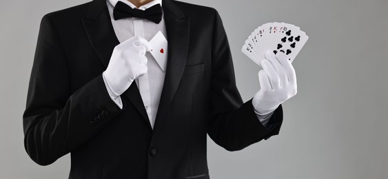 Photo of Illusionist hiding one playing card behind jacket lapel while showing deck on grey background, closeup. Space for text