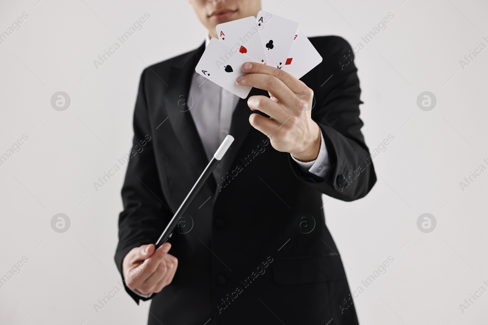 Photo of Illusionist pointing magic wand on playing cards against white background, closeup