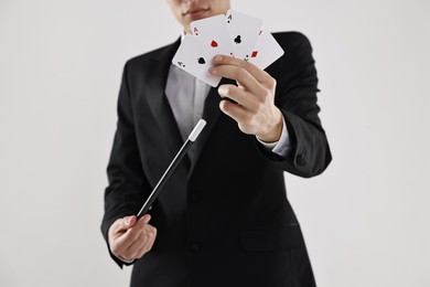 Photo of Illusionist pointing magic wand on playing cards against white background, closeup