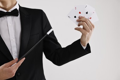 Photo of Illusionist pointing magic wand on playing cards against white background, closeup