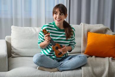 Photo of Happy woman playing ukulele on sofa at home