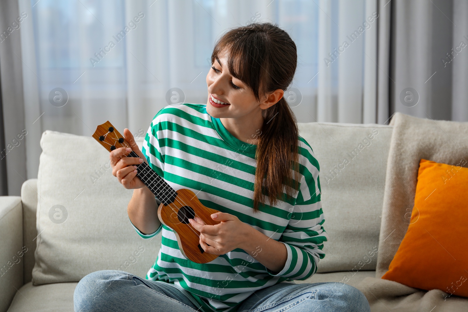 Photo of Happy woman playing ukulele on sofa at home