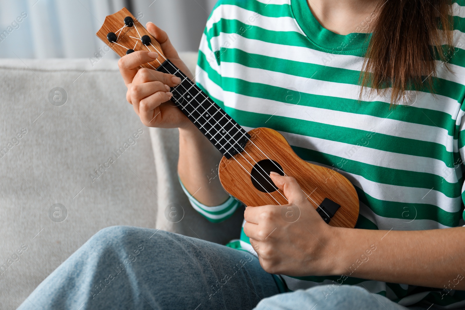 Photo of Woman playing ukulele on sofa at home, closeup