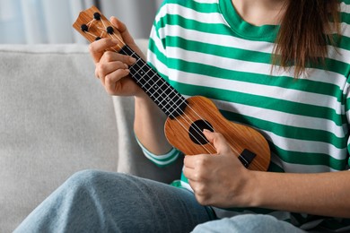 Photo of Woman playing ukulele on sofa at home, closeup