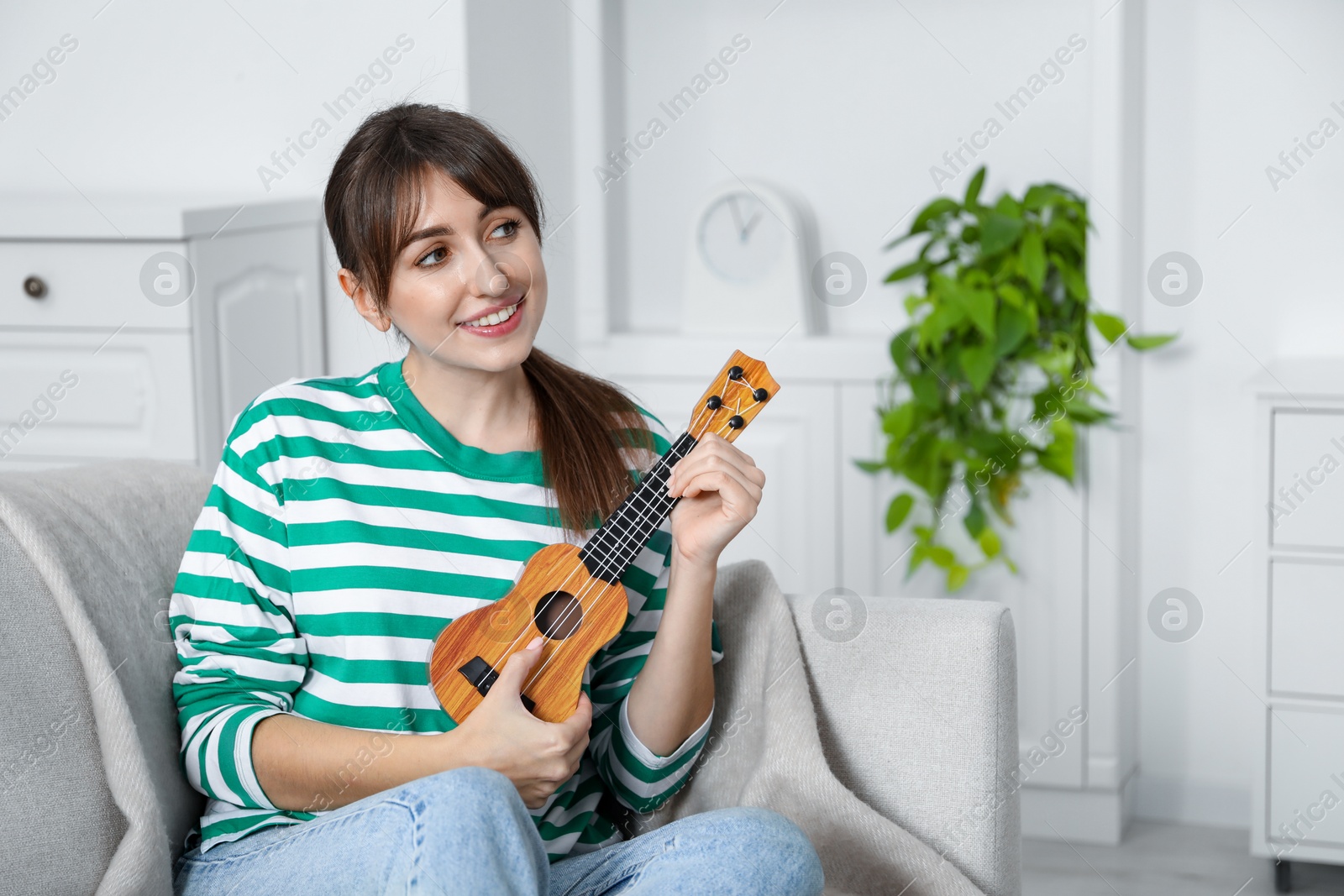 Photo of Happy woman playing ukulele on sofa at home