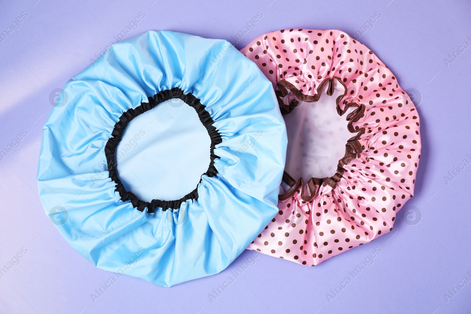 Photo of Two shower caps on lilac background, top view