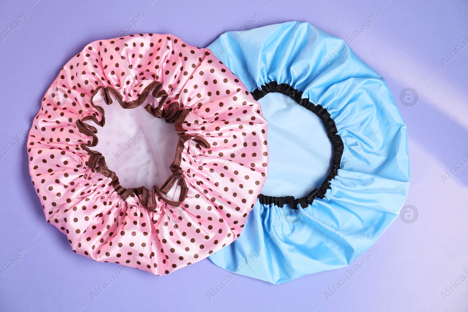 Photo of Two shower caps on lilac background, top view