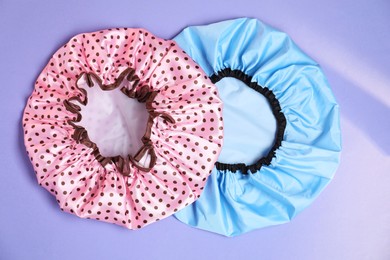 Photo of Two shower caps on lilac background, top view