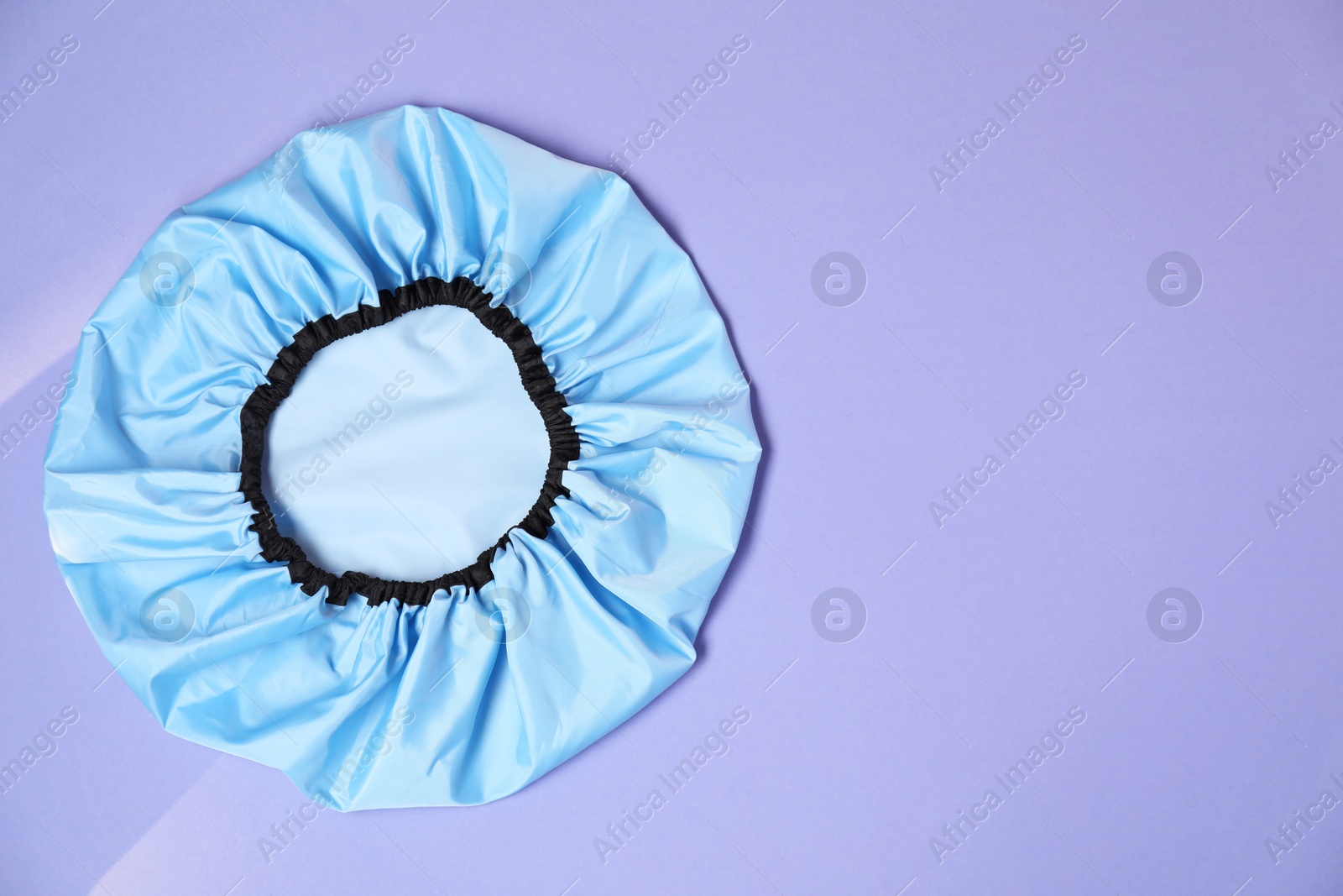 Photo of One shower cap on lilac background, top view. Space for text