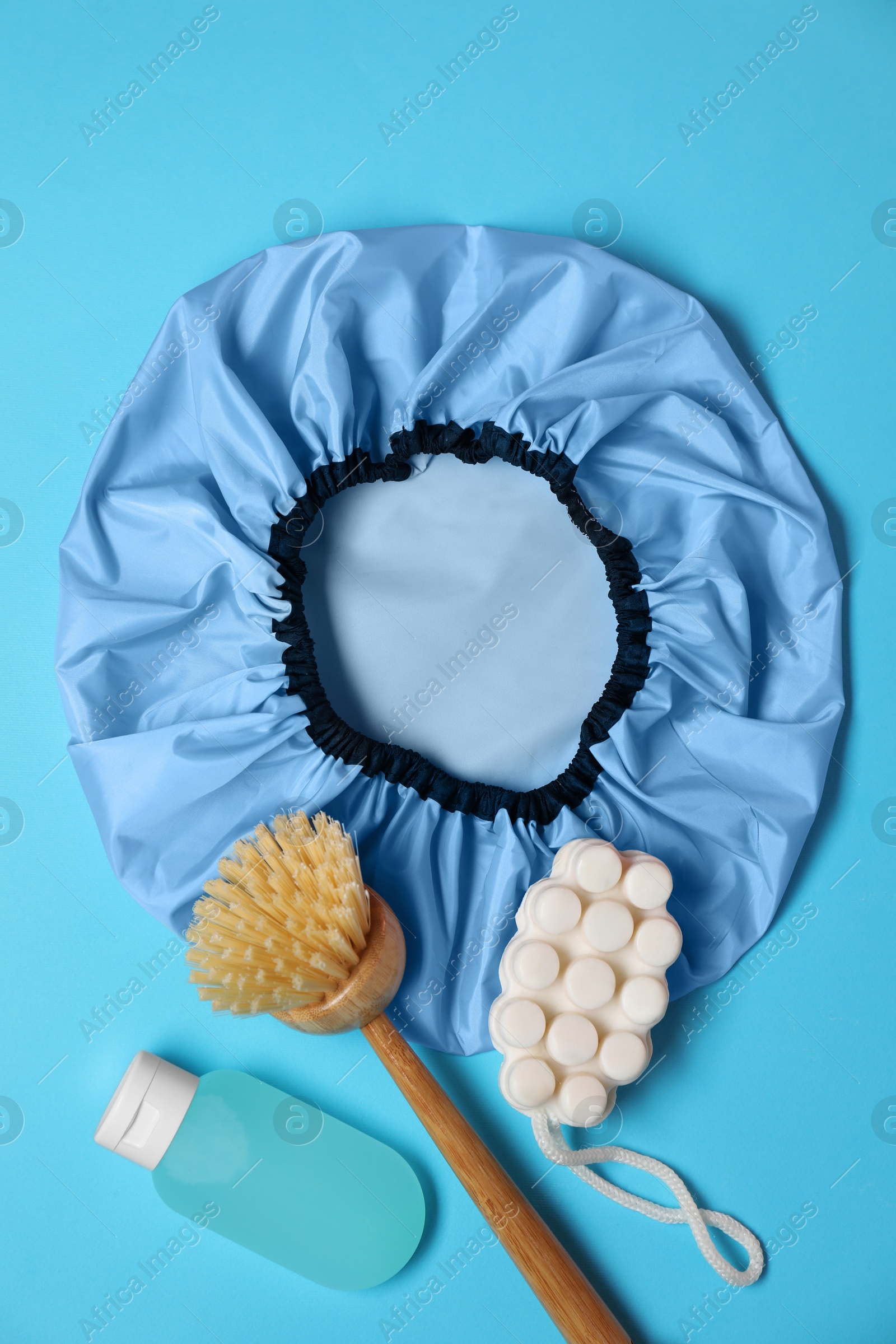 Photo of Shower cap and bath accessories on light blue background, flat lay