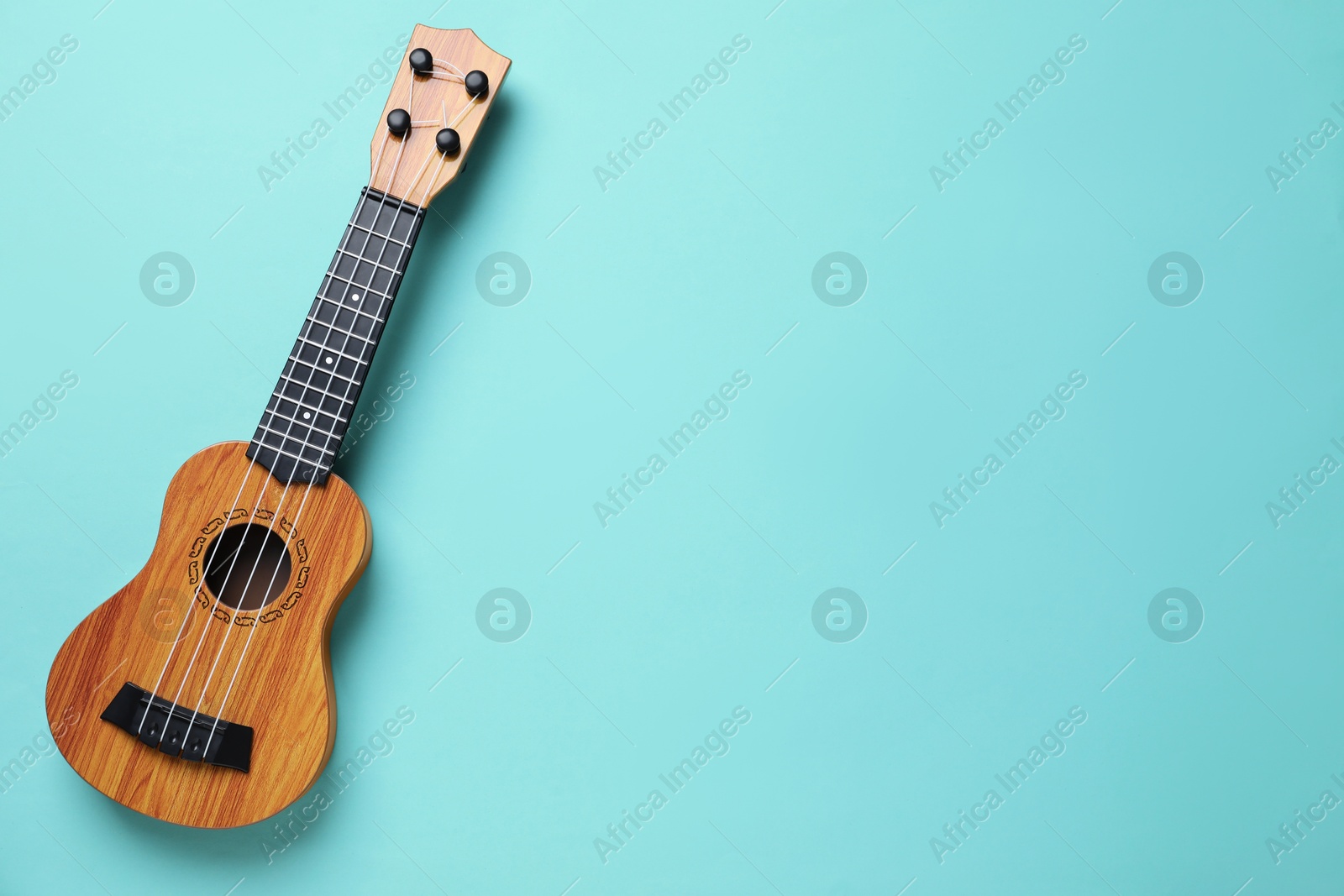 Photo of One ukulele on turquoise background, top view. Space for text