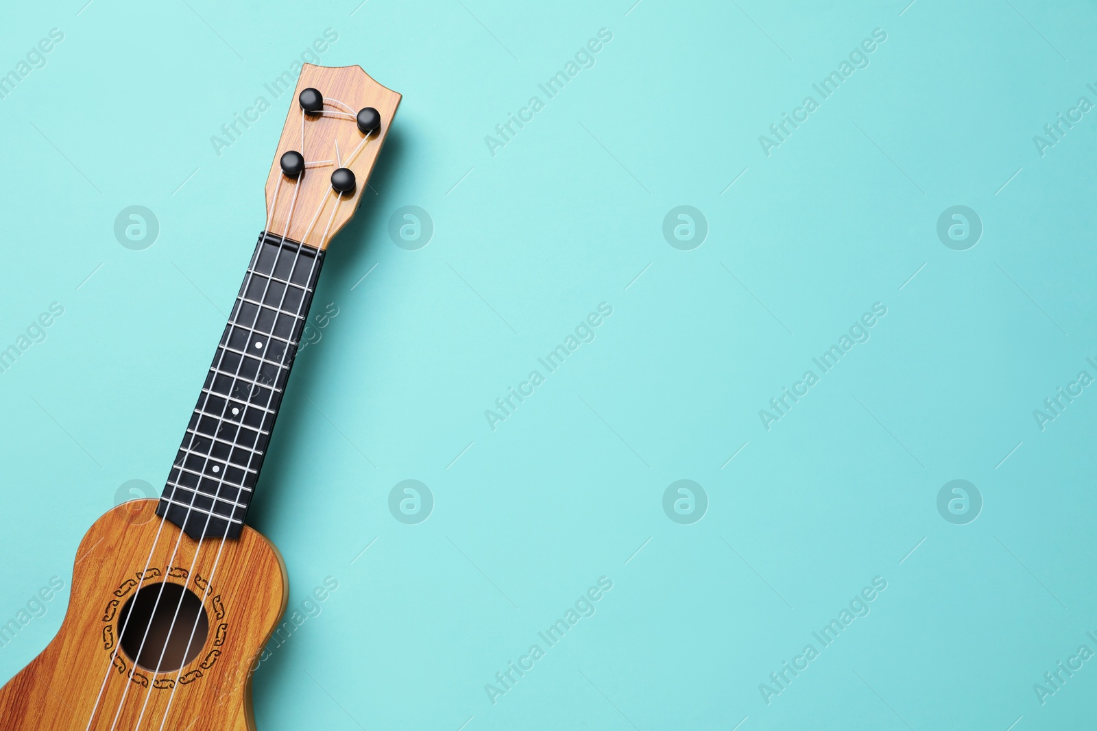 Photo of One ukulele on turquoise background, top view. Space for text