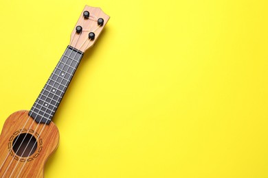 Photo of One ukulele on yellow background, top view. Space for text