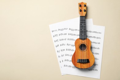 Photo of Ukulele and music sheets on beige background, top view. Space for text