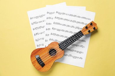 Ukulele and music sheets on yellow background, top view