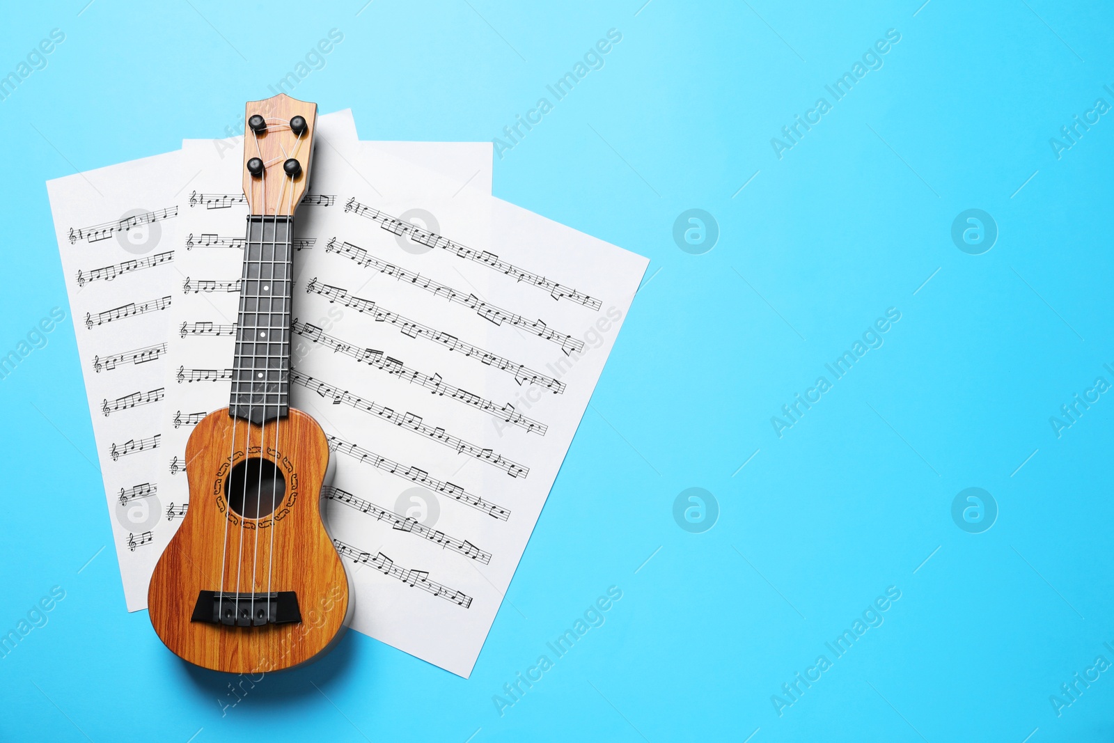 Photo of Ukulele and music sheets on light blue background, top view. Space for text