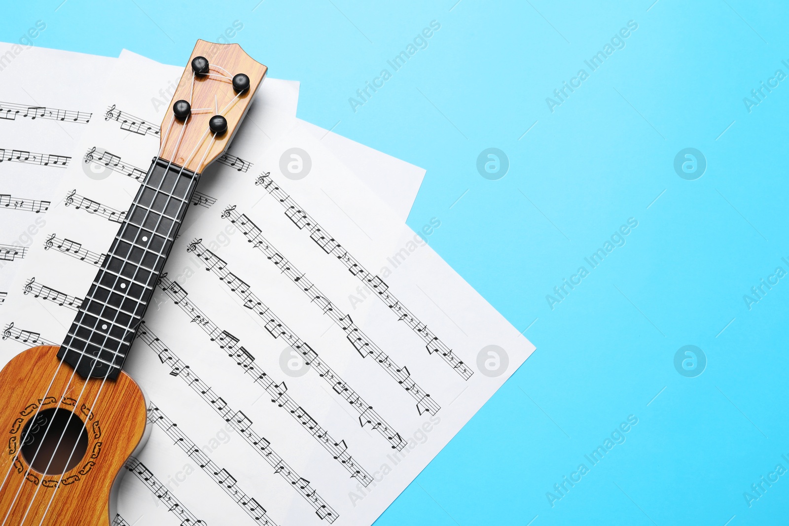 Photo of Ukulele and music sheets on light blue background, top view. Space for text