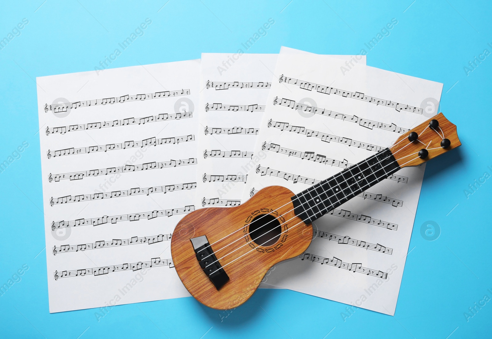 Photo of Ukulele and music sheets on light blue background, top view