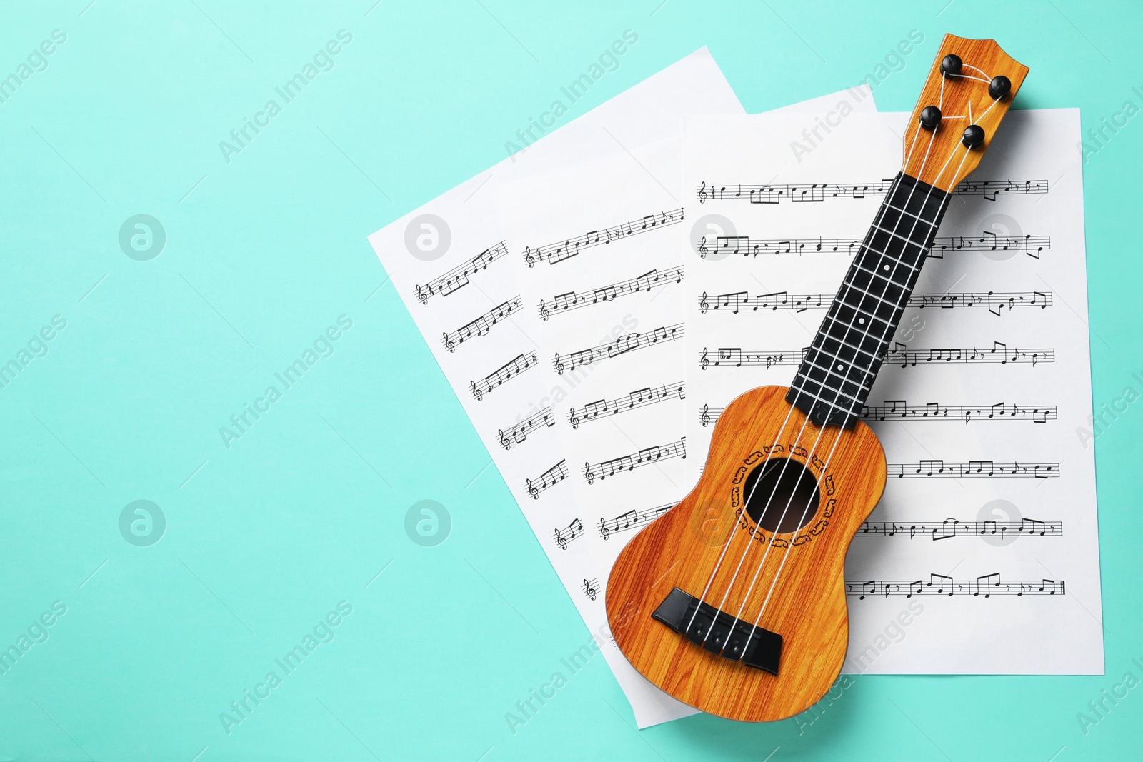 Photo of Ukulele and music sheets on turquoise background, top view. Space for text