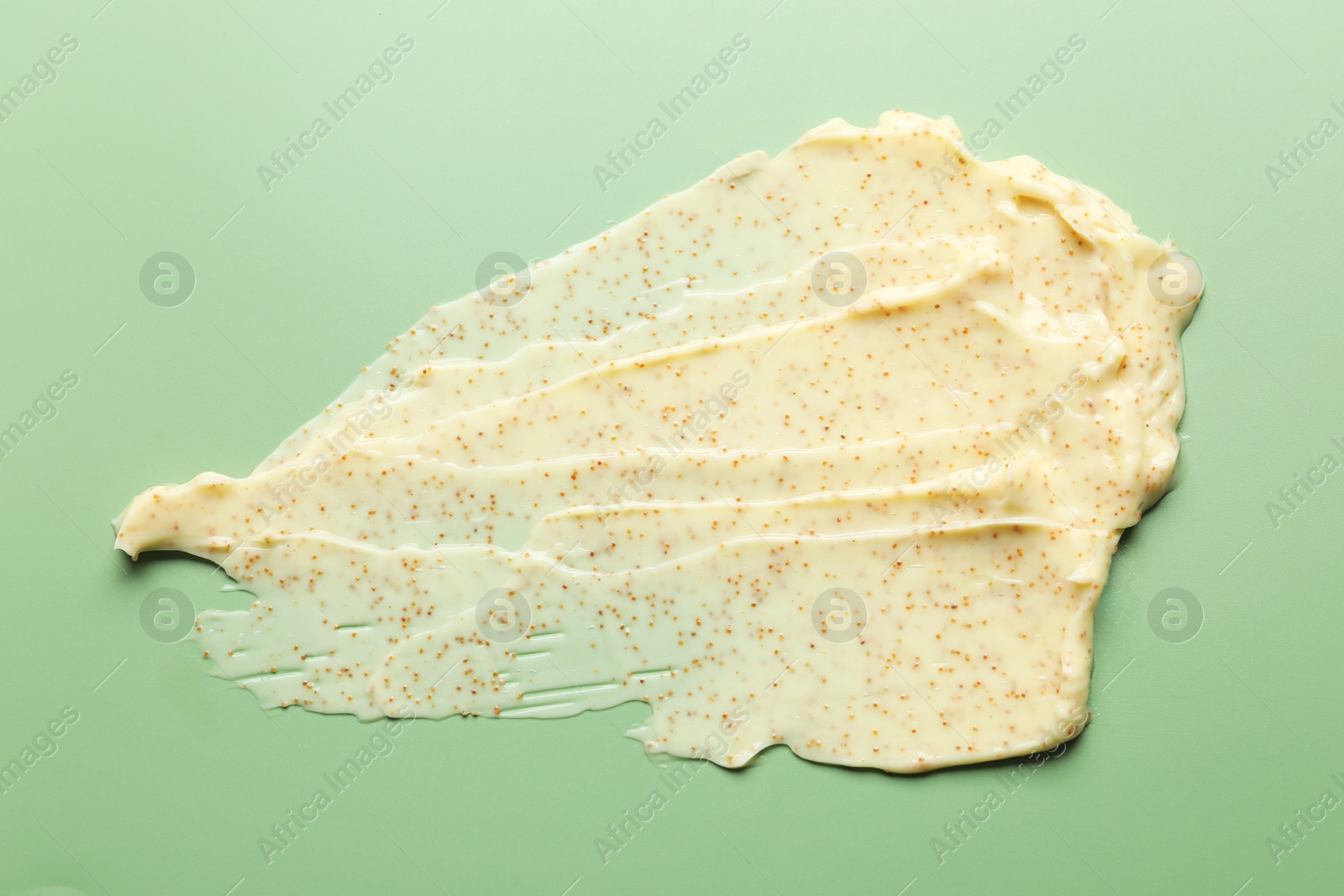 Photo of Smear of body scrub on light green background, top view