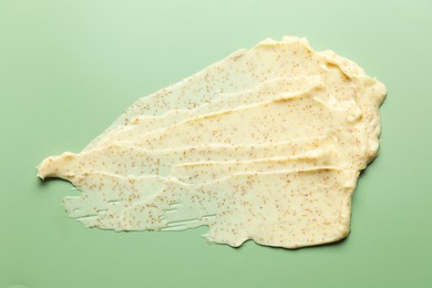 Photo of Smear of body scrub on light green background, top view