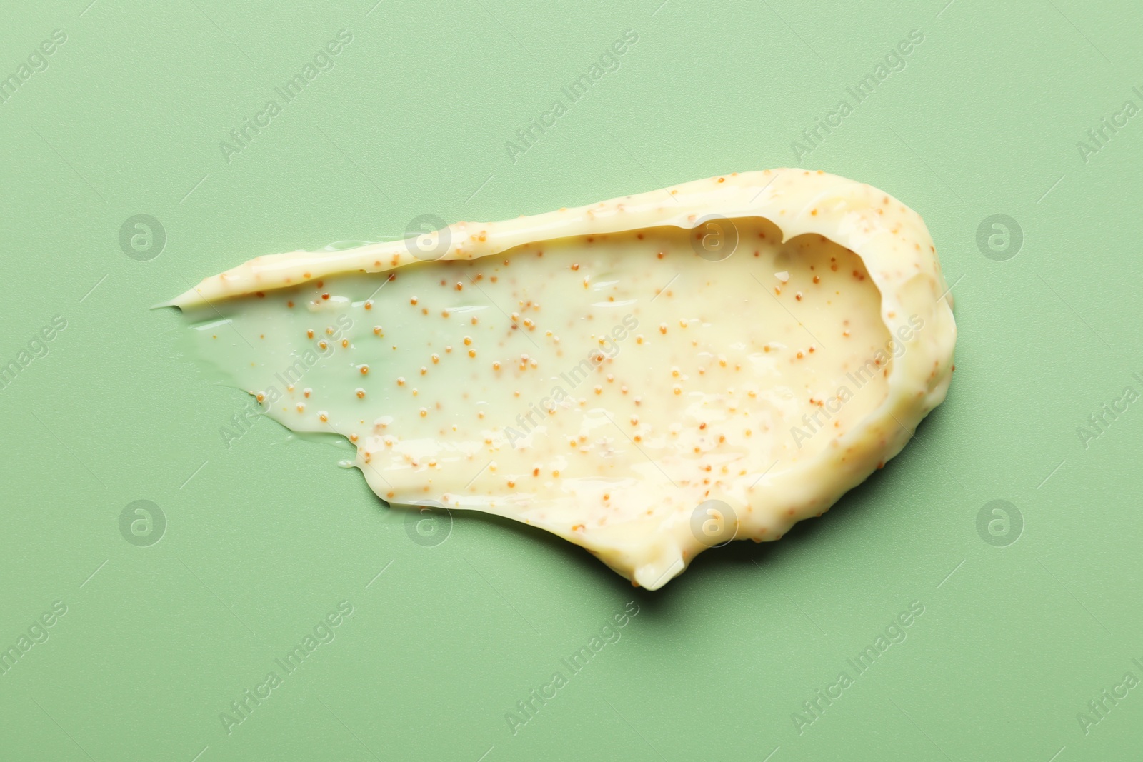 Photo of Smear of body scrub on light green background, top view