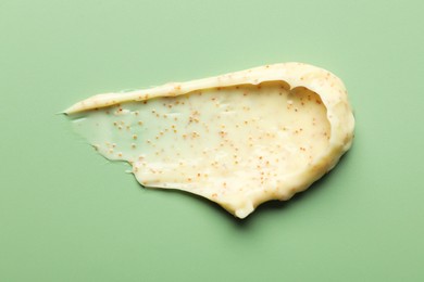 Photo of Smear of body scrub on light green background, top view