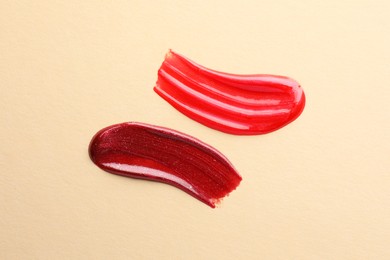 Photo of Lip glosses on beige background, top view. Smears of cosmetic products