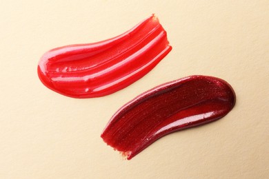 Photo of Lip glosses on beige background, top view. Smears of cosmetic products