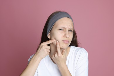 Photo of Upset teenage girl popping pimple on her face against pink background. Acne problem