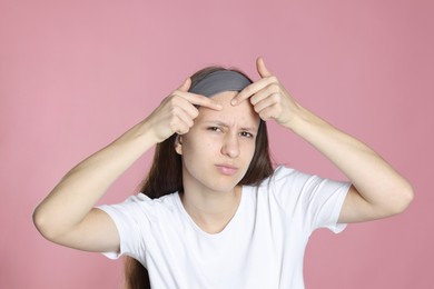 Photo of Upset teenage girl popping pimple on her face against pink background. Acne problem