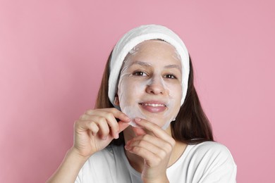 Photo of Teenage girl removing sheet facial mask on pink background. Acne treatment