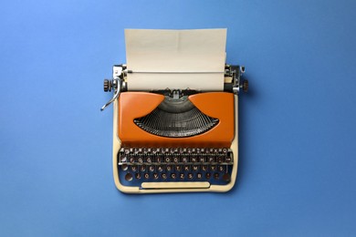 Photo of Vintage typewriter with sheet of paper on blue background, top view