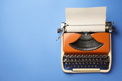 Photo of Vintage typewriter with sheet of paper on blue background, top view. Space for text