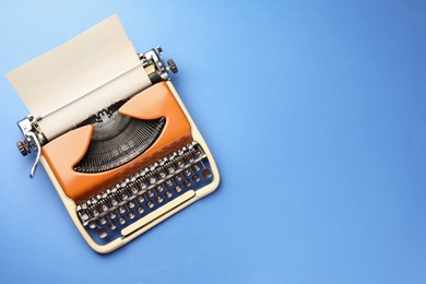 Photo of Vintage typewriter with sheet of paper on blue background, top view. Space for text