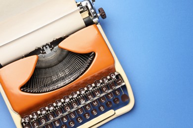 Photo of Vintage typewriter with sheet of paper on blue background, top view. Space for text