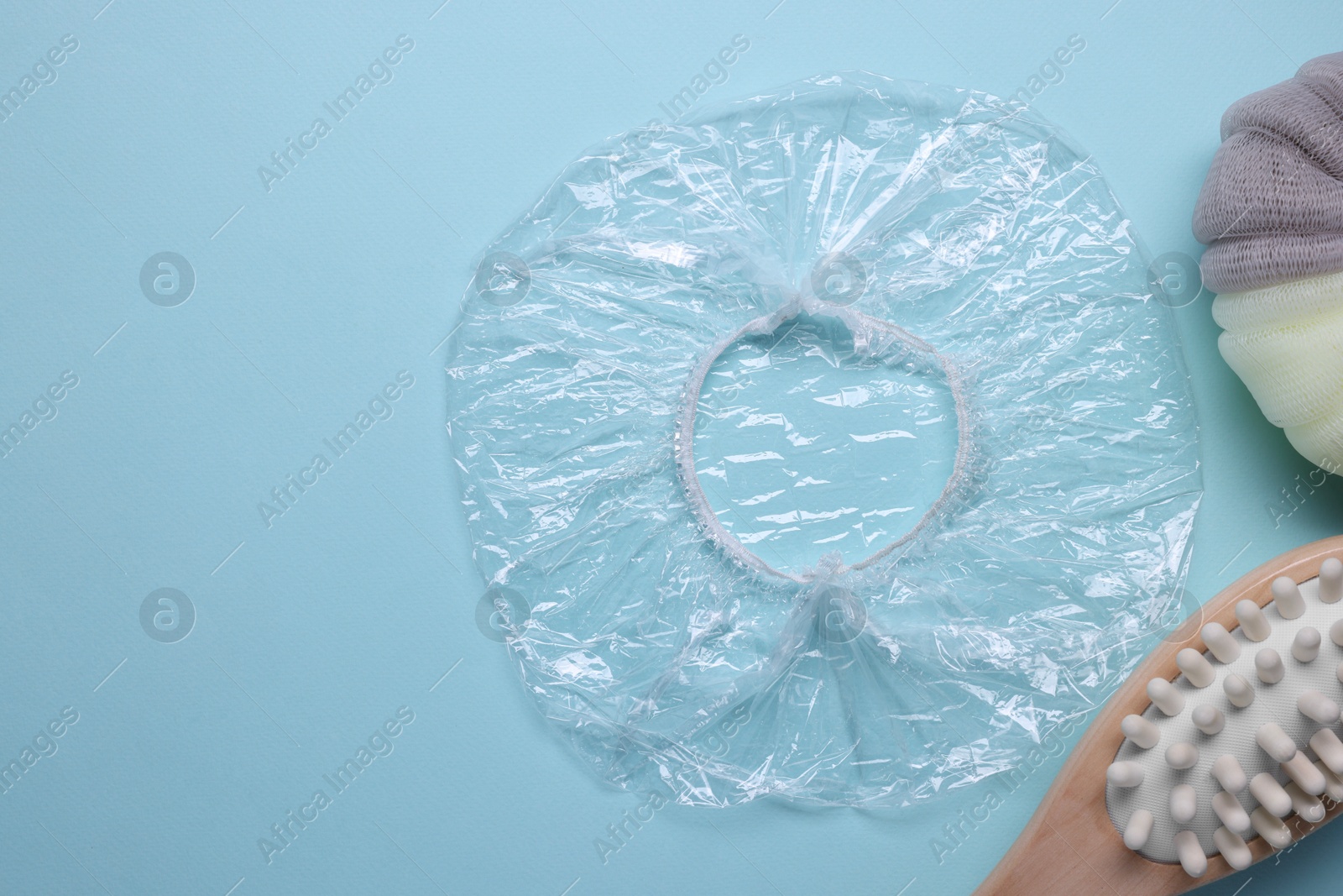 Photo of Shower cap and bath accessories on light blue background, flat lay. Space for text