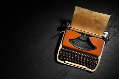 Photo of Vintage typewriter with parchment paper on black background, top view. Space for text
