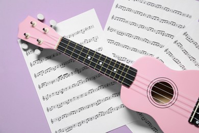 Photo of Ukulele and music sheets on violet background, top view