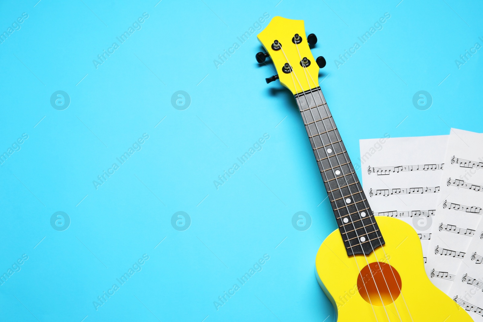 Photo of Ukulele and music sheets on light blue background, top view. Space for text